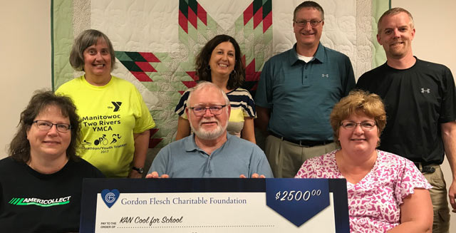 4 people standing and four people sitting behind an oversized check